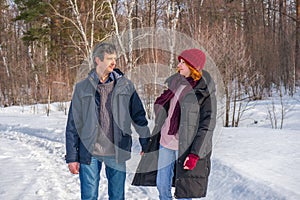 Handsome man and attractive young woman walking along snowy country road in sunny day. Beautiful look, male and female fashion,