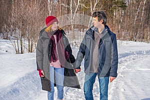 Handsome man and attractive young woman walking along snowy country road in sunny day. Beautiful look, male and female fashion,