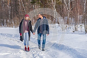 Handsome man and attractive young woman walking along snowy country road in sunny day. Beautiful look, male and female fashion,