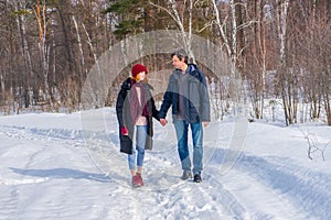 Handsome man and attractive young woman walking along snowy country road in sunny day. Beautiful look, male and female fashion,