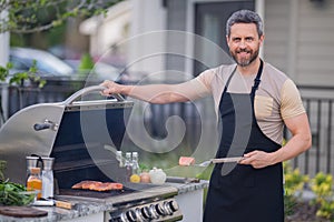 Handsome man barbecue on a grill at backyard. Cooking outdoors and american lifestyle concept. Handsome man preparing