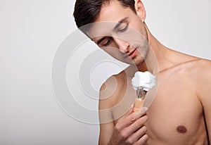 A handsome man with a bare torso is going to apply shaving foam on his face