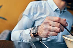 a handsome man with a beard eats borscht in a plate at a table in a cafe and a watch on his hand