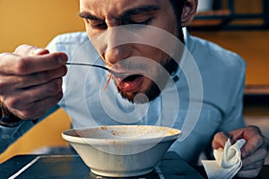 a handsome man with a beard eats borscht in a plate at a table in a cafe and a watch on his hand