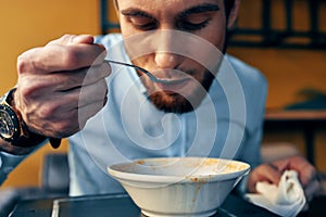 a handsome man with a beard eats borscht in a plate at a table in a cafe and a watch on his hand