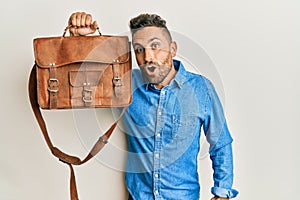 Handsome man with beard holding business bag scared and amazed with open mouth for surprise, disbelief face