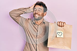 Handsome man with beard holding delivery paper bag with heart reminder smiling confident touching hair with hand up gesture,