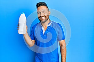 Handsome man with beard holding liter bottle of milk looking positive and happy standing and smiling with a confident smile