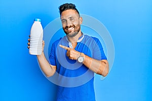 Handsome man with beard holding liter bottle of milk smiling happy pointing with hand and finger