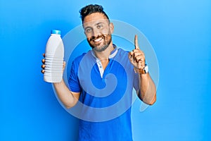 Handsome man with beard holding liter bottle of milk smiling with an idea or question pointing finger with happy face, number one