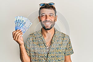 Handsome man with beard holding south african 100 rand banknotes looking positive and happy standing and smiling with a confident