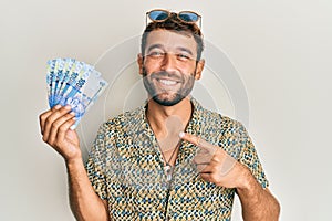 Handsome man with beard holding south african 100 rand banknotes smiling happy pointing with hand and finger