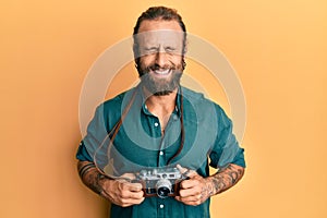 Handsome man with beard and long hair holding vintage camera smiling and laughing hard out loud because funny crazy joke