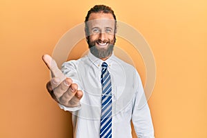 Handsome man with beard and long hair wearing business clothes smiling friendly offering handshake as greeting and welcoming