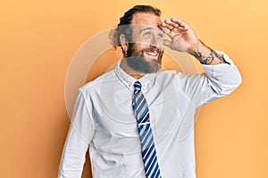 Handsome man with beard and long hair wearing business clothes very happy and smiling looking far away with hand over head