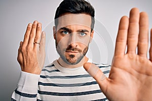 Handsome man with beard showing alliance ring marriage on finger over white background with open hand doing stop sign with serious