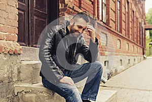 A handsome man with beard sitting on steps outside wearing a je