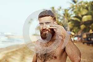 Handsome Man with beard, In Sunglasses Sunbathing With Sunscreen Lotion Body In Summer. Male Fitness Model Tanning Using Solar Blo