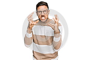 Handsome man with beard wearing casual clothes and glasses shouting frustrated with rage, hands trying to strangle, yelling mad