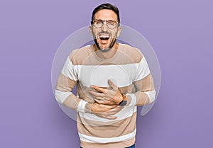 Handsome man with beard wearing casual clothes and glasses smiling and laughing hard out loud because funny crazy joke with hands