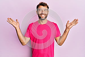 Handsome man with beard wearing casual pink tshirt over pink background celebrating victory with happy smile and winner expression