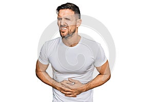 Handsome man with beard wearing casual white t shirt with hand on stomach because nausea, painful disease feeling unwell