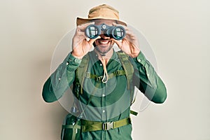 Handsome man with beard wearing explorer hat looking through binoculars winking looking at the camera with sexy expression,