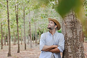 Handsome man with beard in white shirt leaning against a tree and smiling for the camera.