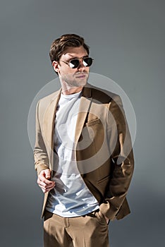 Handsome man in beige suite with hand in pocket looking away on grey.