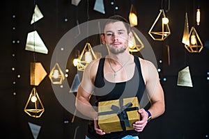 Handsome man in black tank top holds a gift in her hands, opens a gift, present