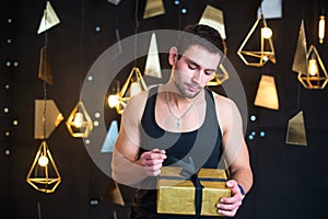 Handsome man in black tank top holds a gift in her hands, opens a gift, present