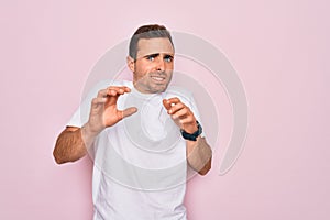 Handsome man with blue eyes wearing casual white t-shirt standing over pink background disgusted expression, displeased and