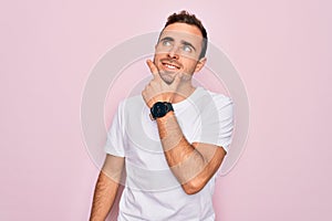 Handsome man with blue eyes wearing casual white t-shirt standing over pink background with hand on chin thinking about question,