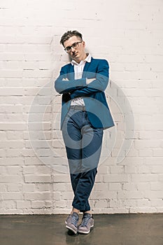 Handsome man in blue jacket and spectacles posing outdoor by a white brick wall. Men`s beauty, fashion. Business style.