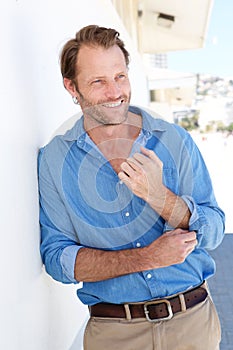 Handsome man in blue shirt leaning against wall outside
