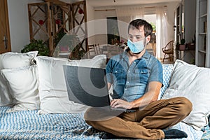 Handsome man with blue shirt and a medical mask, telecommuting or writing on his laptop