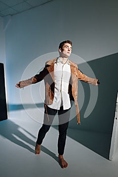 Handsome man in a brown jacket spreads his arms to the sides on a gray background top view