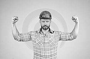 handsome man builder in construction safety helmet and checkered shirt demonstarte power on building site, male strength