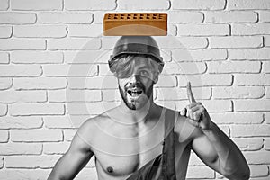 Handsome man builder with sexy muscular athletic strong body. Hard hat or helmet holds brick on white brick wall