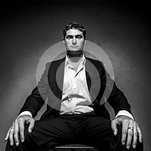 Handsome man in a business suit sitting on a chair, black and white portrait, low angle shot