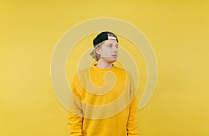 Handsome man in cap and yellow sweatshirt isolated on yellow background and looks away with a serious face