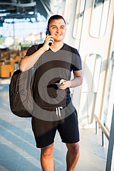 Handsome man in casual wear talking on his mobile phone while siting in the hall of the airport