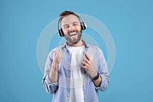 Handsome man with cellphone listening to music in headphones, singing along to his favorite song on blue background
