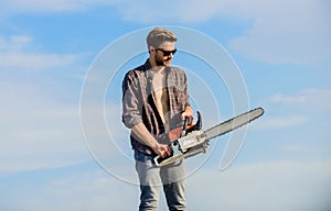 Handsome man with chainsaw blue sky background. Gardener lumberjack equipment. Lumberjack with chainsaw in his hands