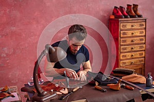 Handsome man concentrated on cutting the cloth for shoes