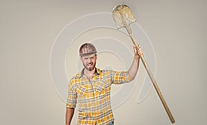 handsome man contractor in construction safety helmet and checkered shirt on building site with shovel, labor day