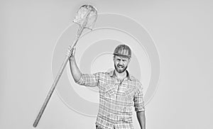 handsome man contractor in construction safety helmet and checkered shirt on building site with shovel, labor day