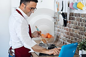 Handsome man cooking while following a recipe on the digital tablet in the kitchen at home