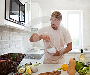 Handsome man cooking at home preparing salad in kitchen