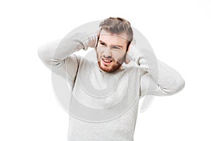 Handsome man covering ears because of loud noise over white background. Guy can`t stand the sound isolated